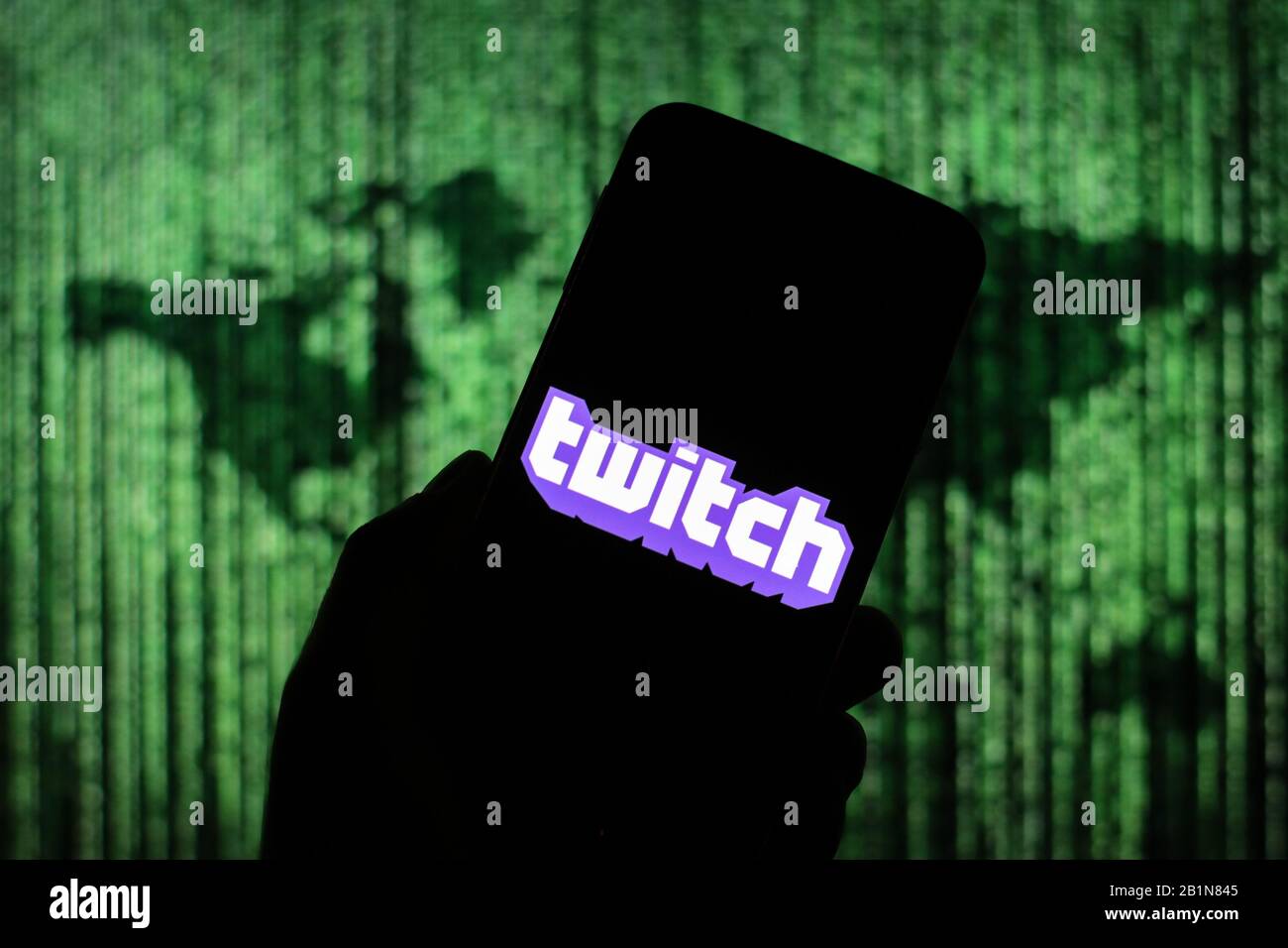 Le logo du site Web de diffusion en continu TWitch est affiché sur l'écran du smartphone avec une carte du monde de type matrice visible floue en arrière-plan Banque D'Images