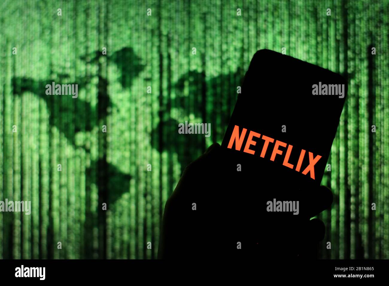 Logo Netflix affiché sur l'écran du smartphone avec une carte du monde de type matrice visible floue en arrière-plan Banque D'Images
