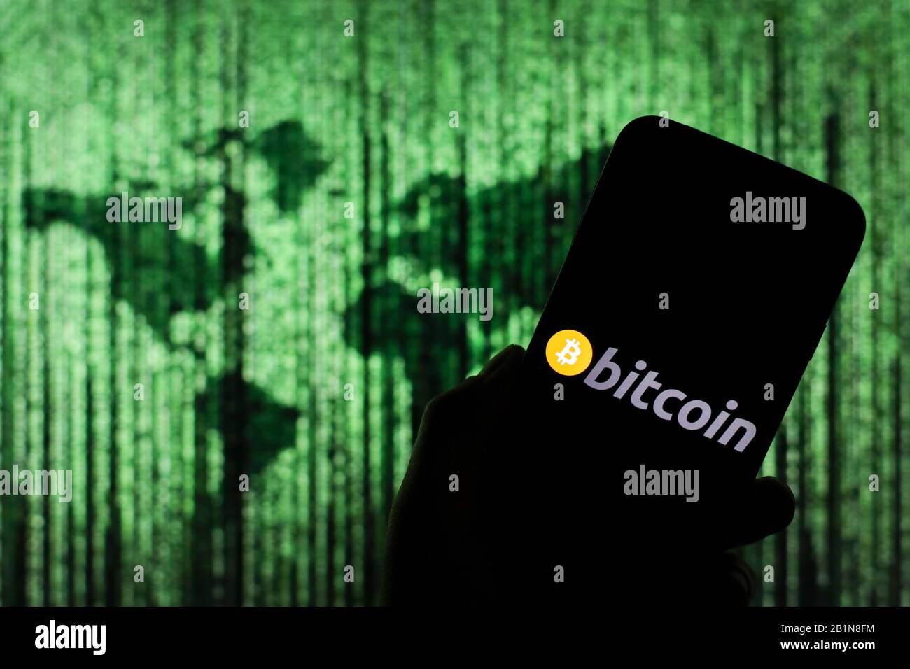 Logo Bitcoin crypto-monnaie visible sur l'écran du smartphone avec une carte du monde de type matrice visible floue en arrière-plan Banque D'Images