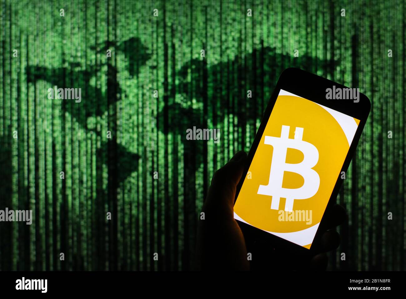 Logo Bitcoin crypto-monnaie visible sur l'écran du smartphone avec une carte du monde de type matrice visible floue en arrière-plan Banque D'Images
