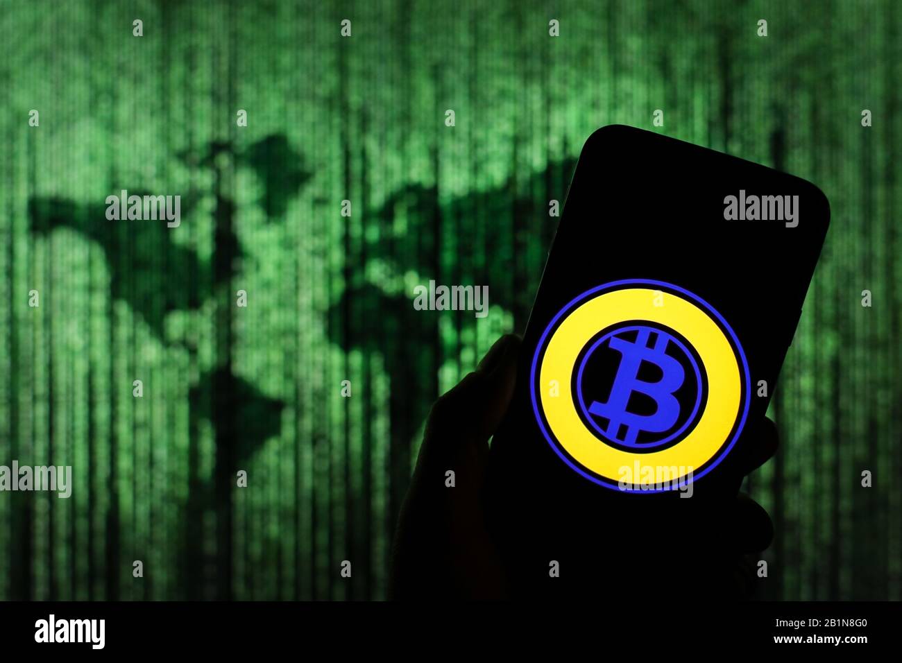 Logo Bitcoin crypto-monnaie visible sur l'écran du smartphone avec une carte du monde de type matrice visible floue en arrière-plan Banque D'Images