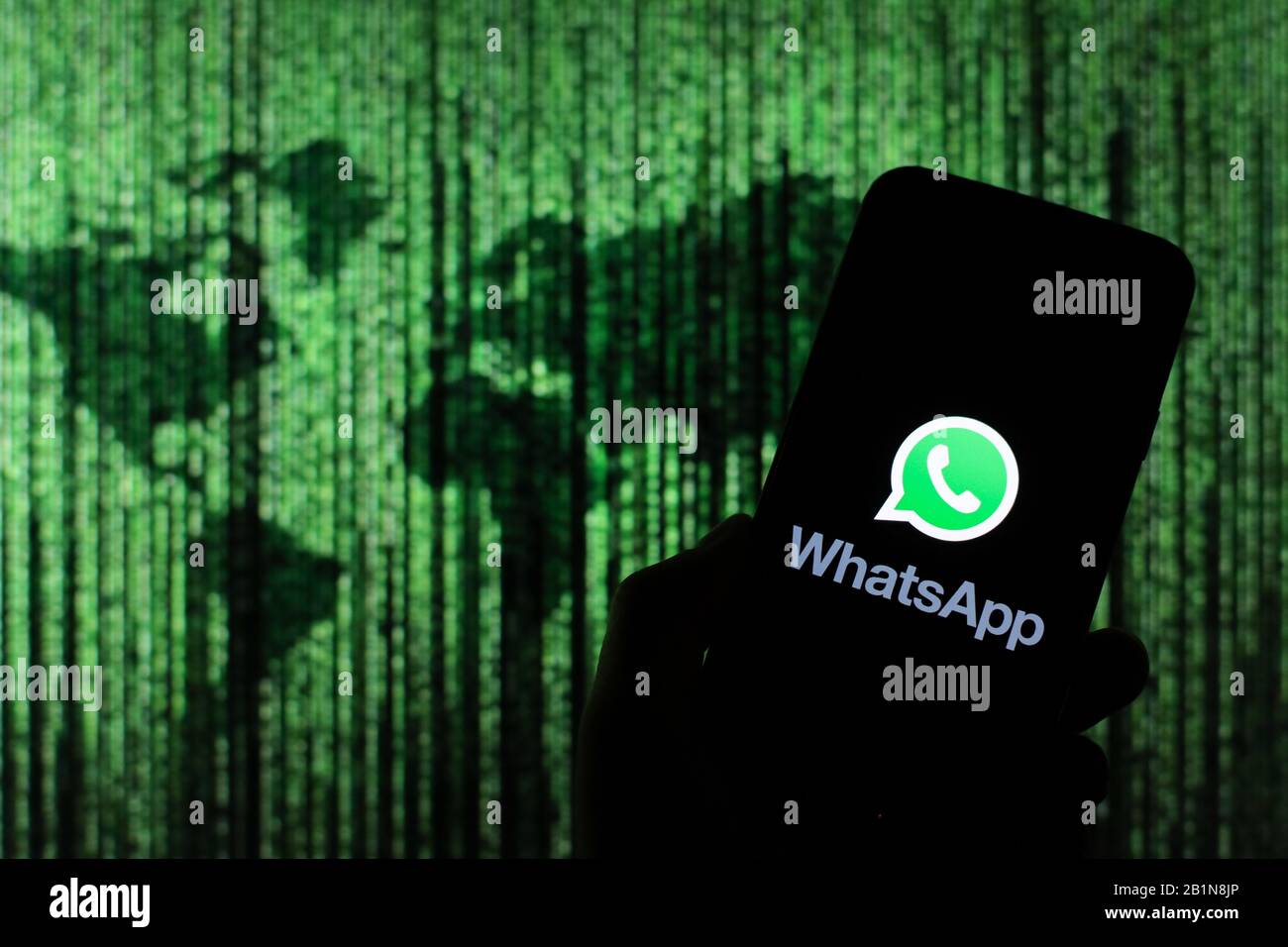 Le logo de l'application WhatsApp Messenger s'affiche sur l'écran du smartphone avec une carte du monde de type matrice visible floue en arrière-plan Banque D'Images