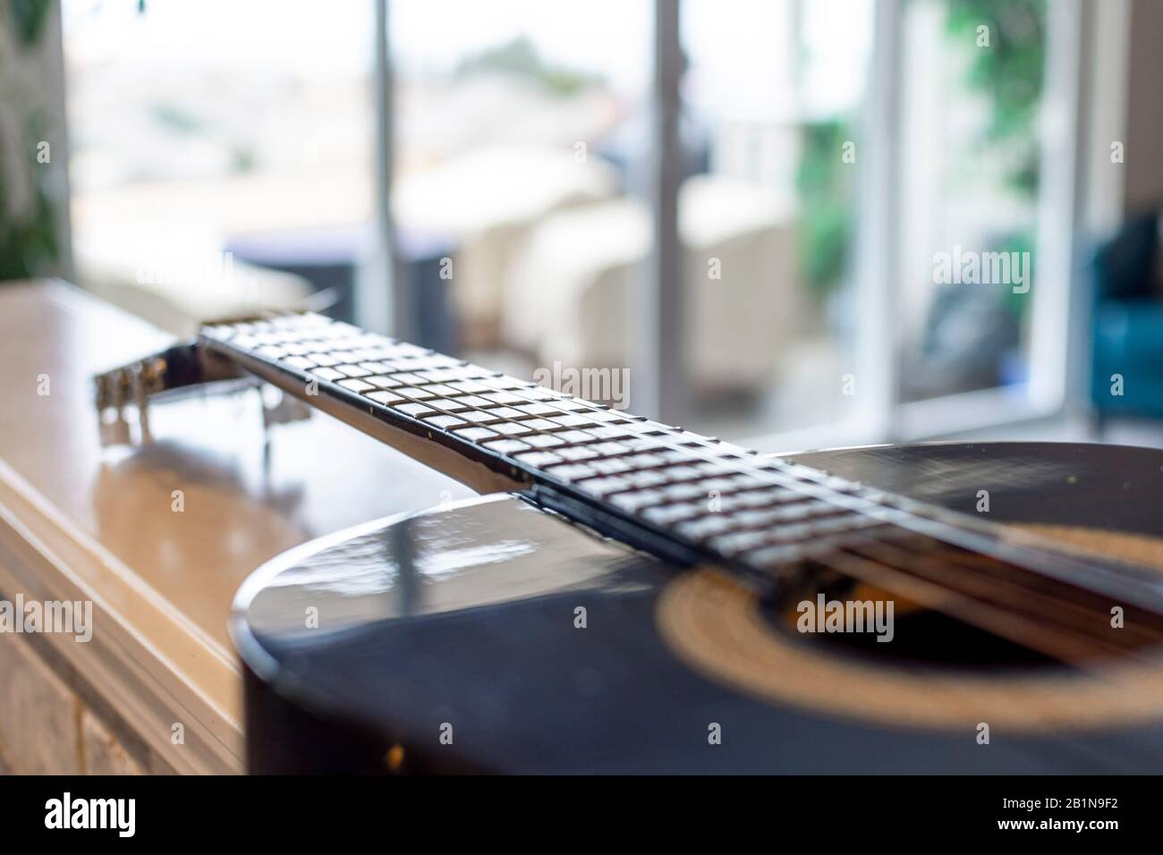 Focalisation sélective sur le cou, les frettes et les cordes d'une guitare acoustique avec fond bokeh flou d'un patio extérieur ensoleillé Banque D'Images
