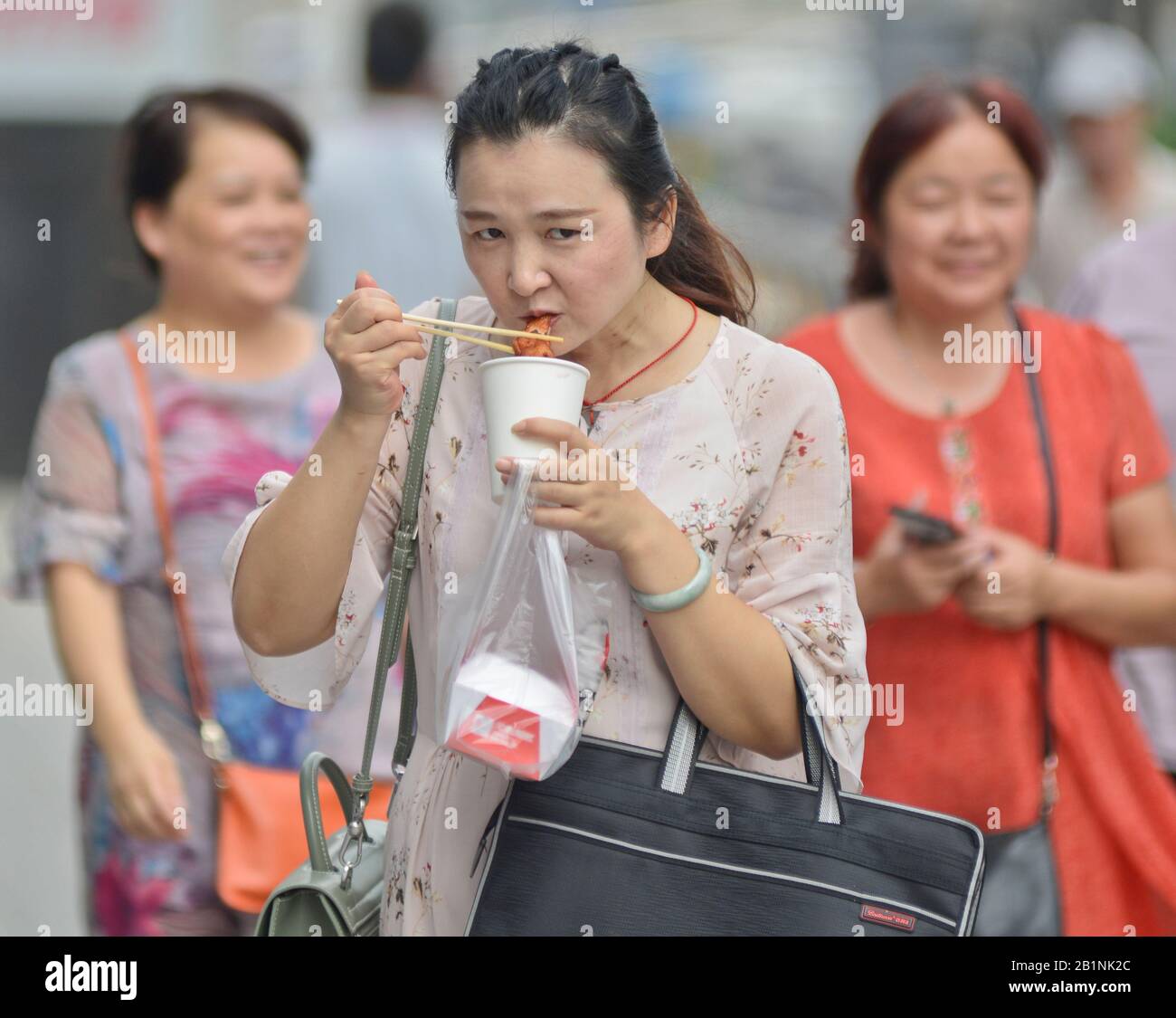 Wuhan: Une femme chinoise mangeant avec des baguettes tout en marchant dans la rue à la sortie de la station de métro Chuhe Hanije, rue Zhong Boi lu. Chine Banque D'Images