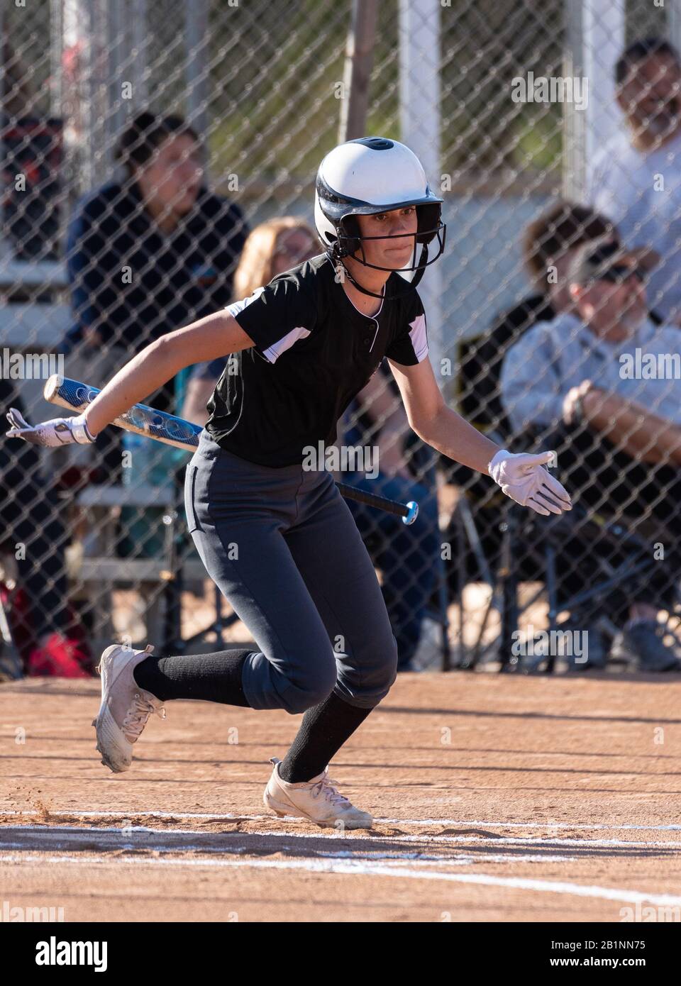 Le joueur de softball féminin de l'école secondaire a mis la chauve-souris de côté pendant qu'elle postule pour faire monter la première ligne de base. Banque D'Images
