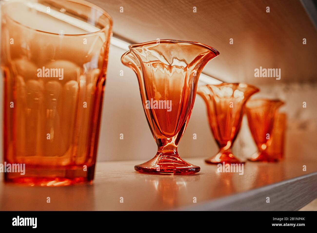 des verres texturés et des vases en verre orange brillant identiques pour les boissons se tiennent sur des étagères en bois à l'intérieur de la chambre Banque D'Images