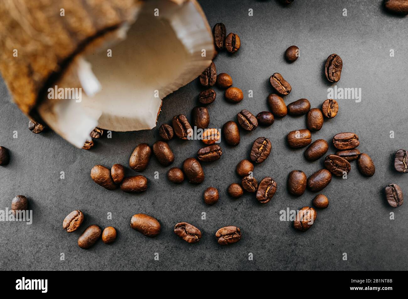 grains sombres frits épars de café arabica et noix de coco mûres cassées sur un fond uniforme dans le style de noir total minimal Banque D'Images