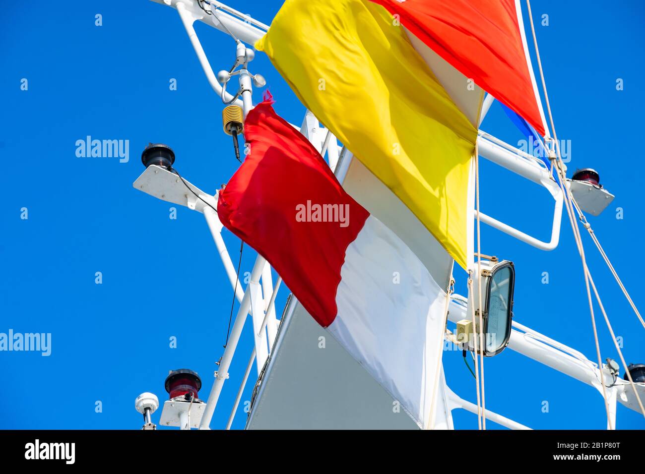 Les drapeaux de quarantaine et les drapeaux pilotes volaient sous des vents forts un jour bleu sur un bateau de croisière avec des feux de navigation en arrière-plan Banque D'Images