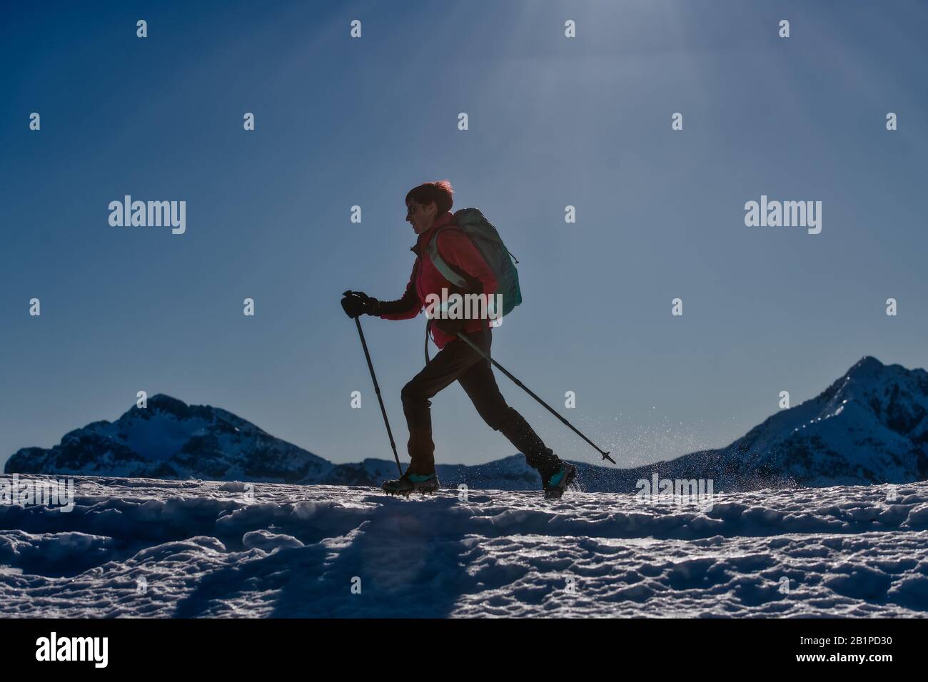 Une femme sportive marche sur la neige avec des crampons et des bâtons Banque D'Images