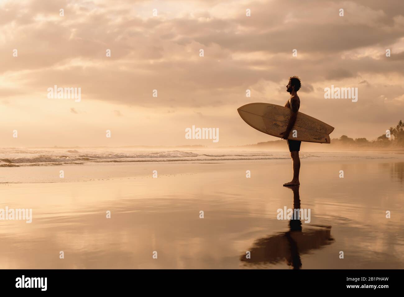 Un agréable surfeur se tient sur la plage au coucher du soleil sur l'océan. Bali surf Banque D'Images