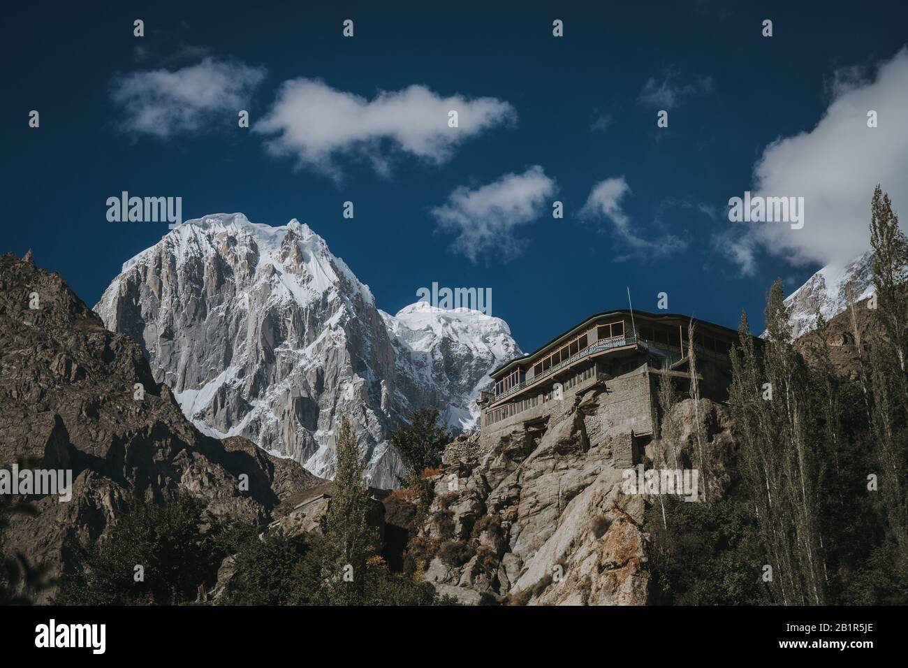 Monastère de falaises dans la vallée de Hunza, au Pakistan, avec une toile de fond spectaculaire de hauts sommets enneigés de montagne sous un ciel bleu Banque D'Images