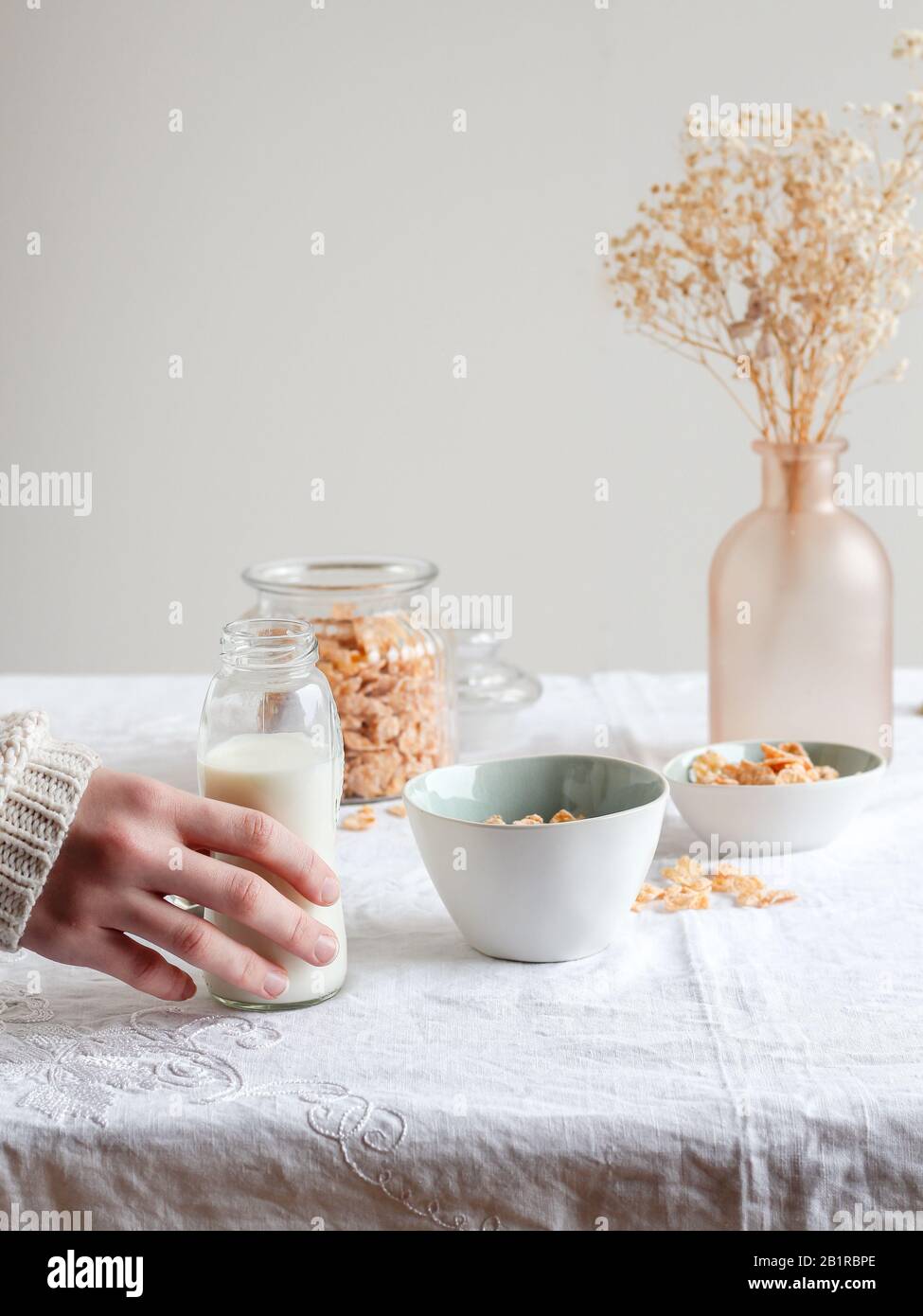Main de femme tenant une bouteille de lait et un bol avec des cornflakes sur une table de petit-déjeuner Banque D'Images