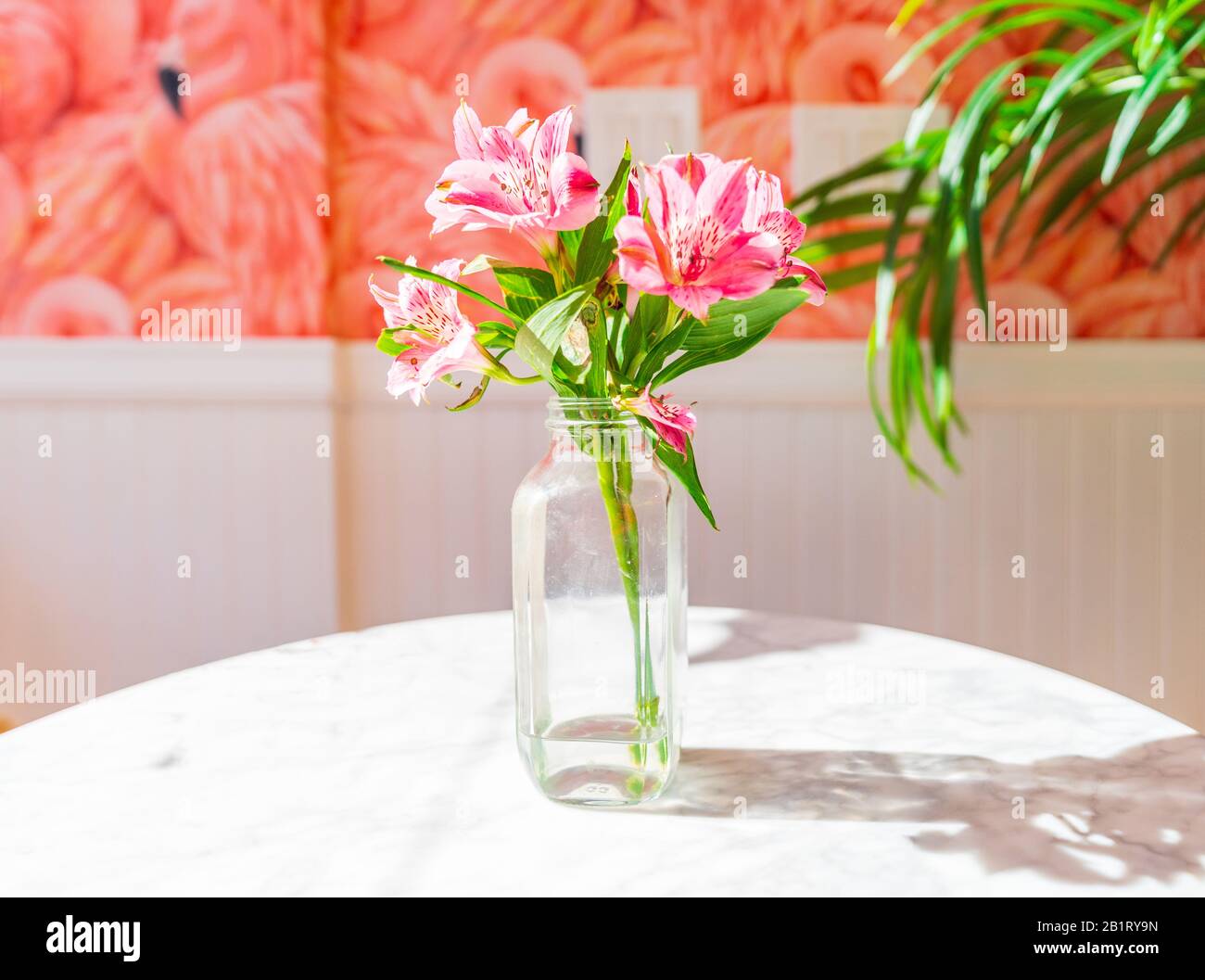 Disposition colorée des fleurs dans un vase en verre et un papier peint Flamingo. Banque D'Images
