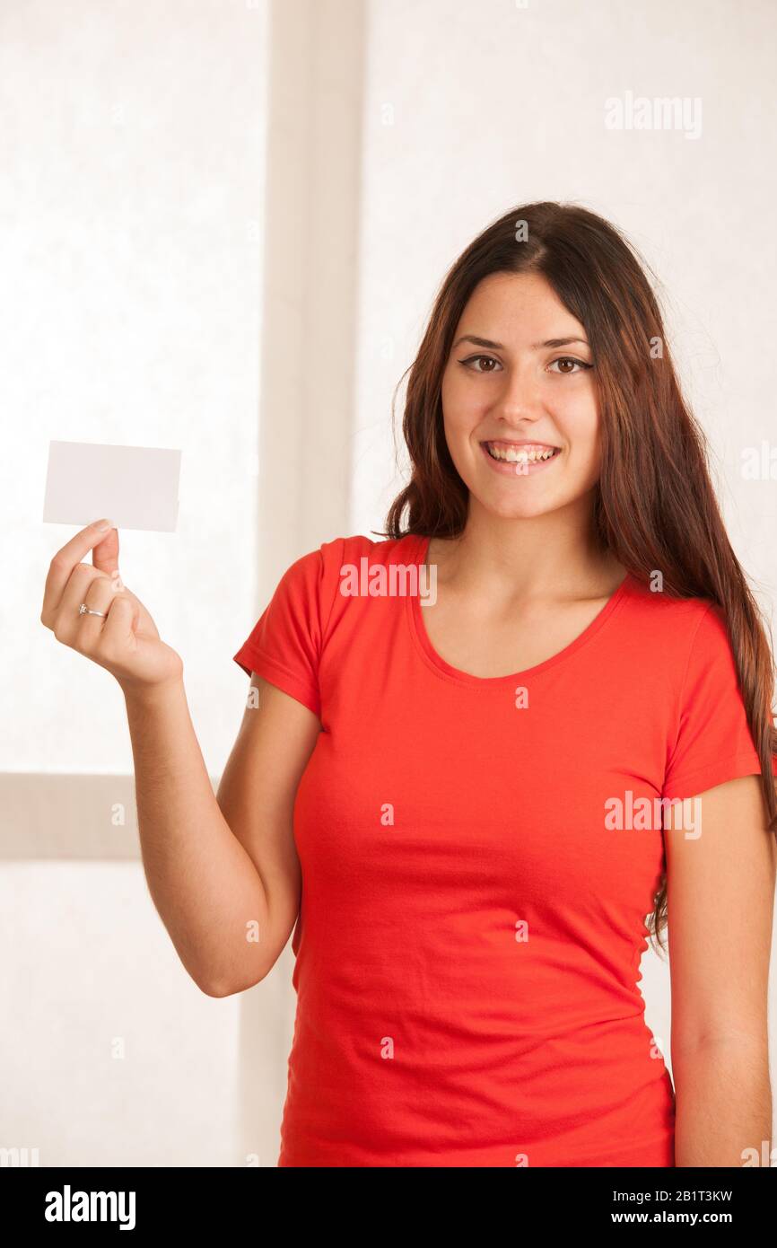Belle jeune femme en t-shirt rouge tient une carte vierge sur fond blanc. Banque D'Images
