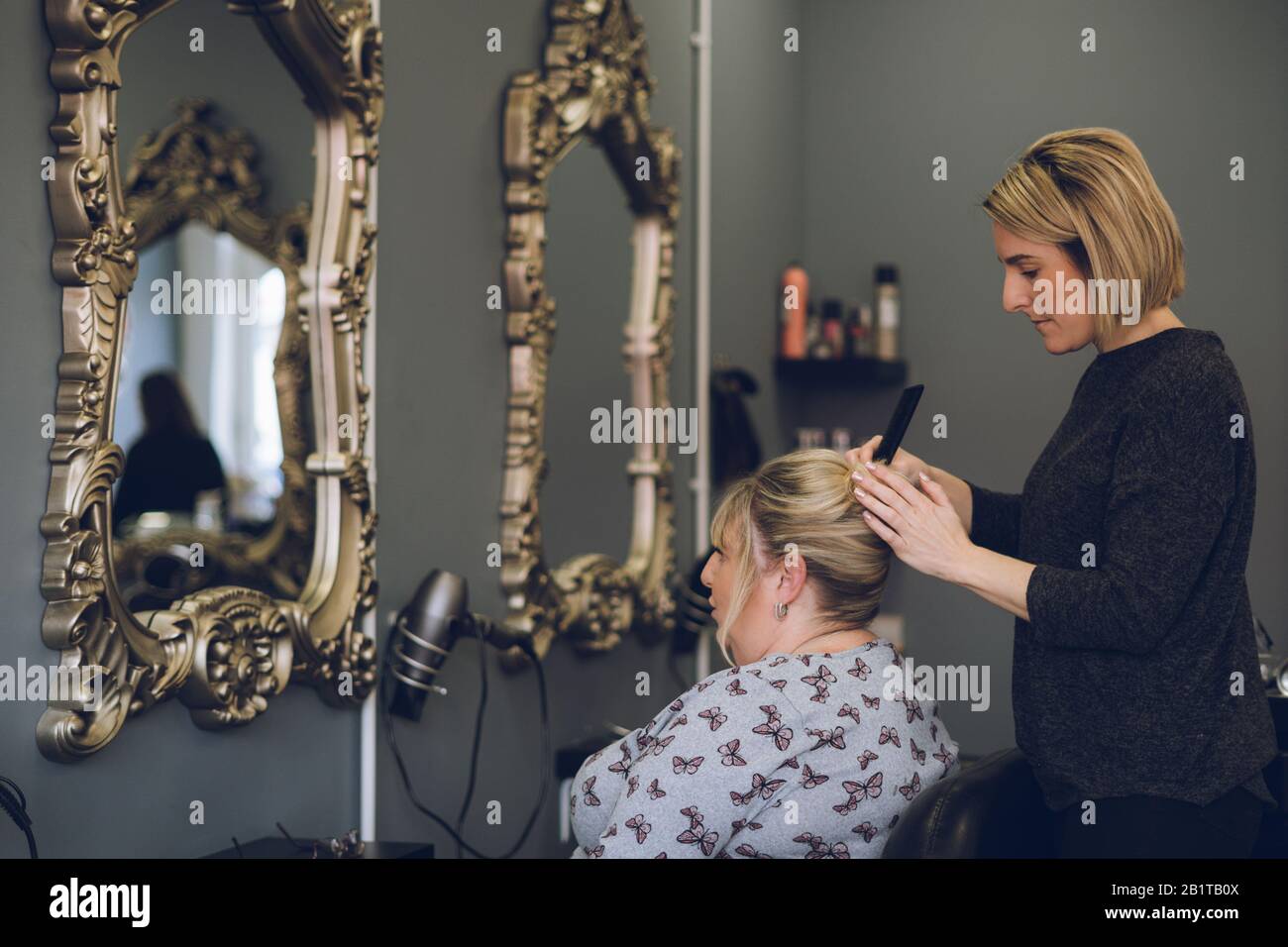 Un coiffeur coiffant les cheveux d'une femme d'âge moyen dans un salon de coiffure ou un salon de coiffure Banque D'Images