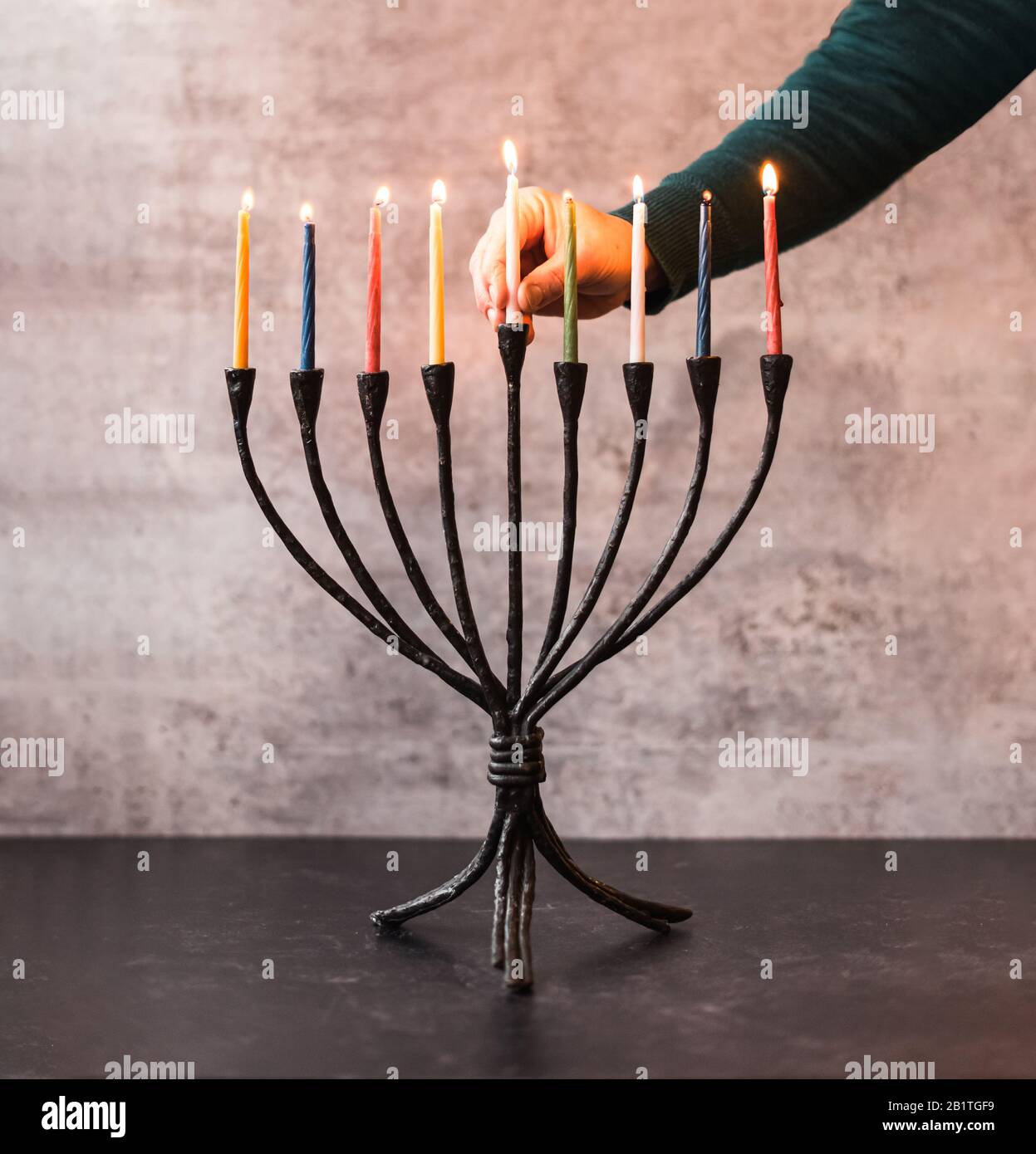 Main de femme plaçant une bougie allumée dans une menorah pour Hanoukkah. Banque D'Images