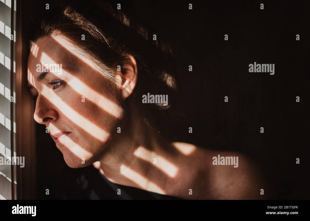 Portrait d'une femme regardant par la fenêtre avec des ombres sur son visage. Banque D'Images