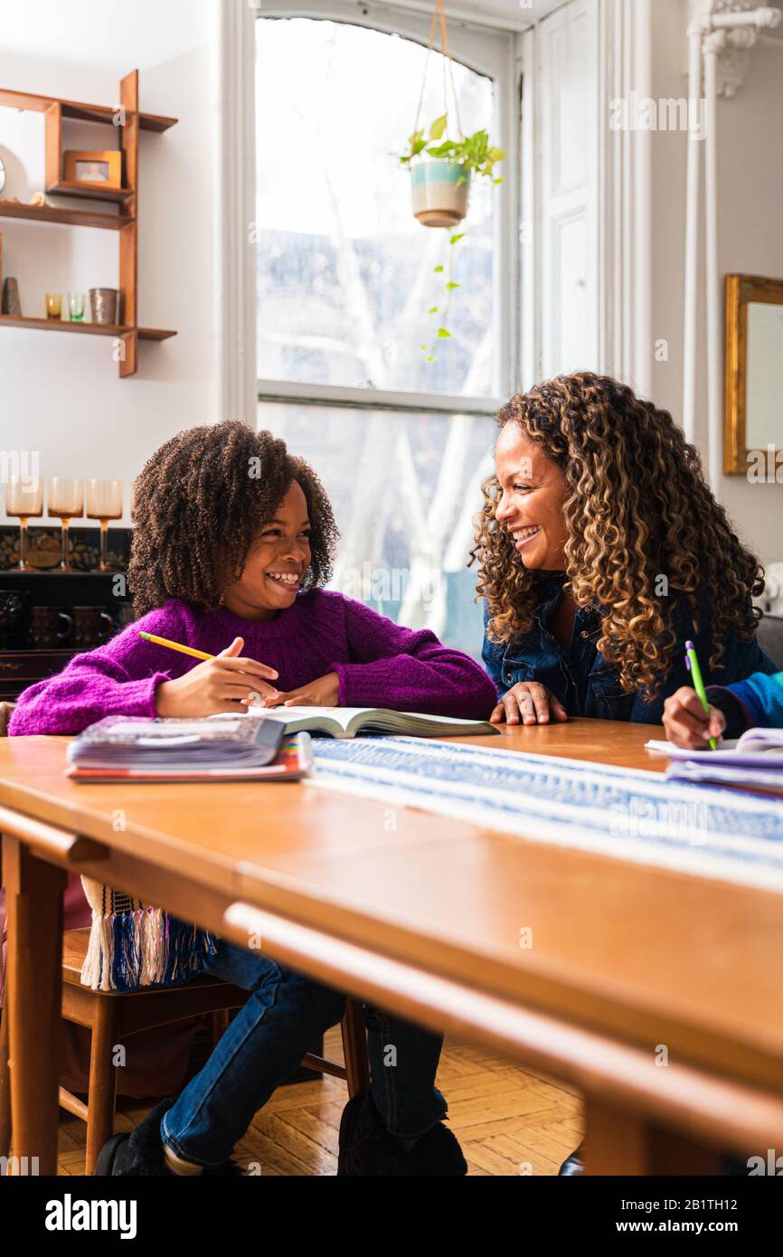 Fille souriante regardant la mère tout en étudiant à la maison Banque D'Images