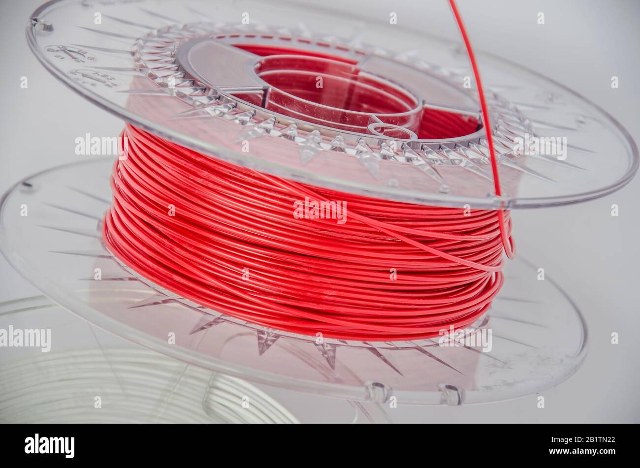 Vue rapprochée du plastique pour l'impression en trois dimensions. Filament en plastique rouge, bobine rouge ABS/PLA pour imprimante tridimensionnelle sur fond blanc, isolé Banque D'Images