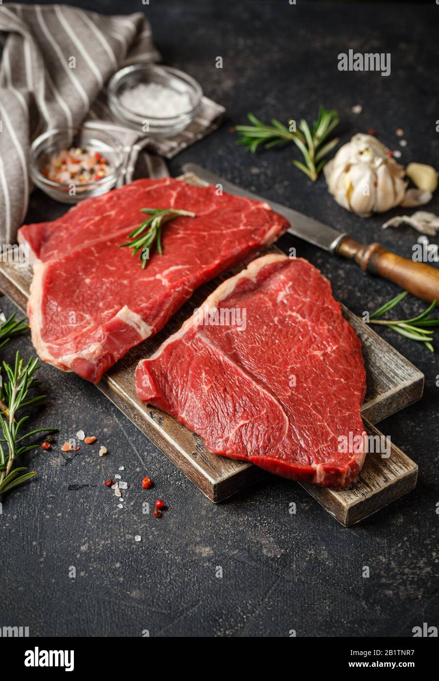 Deux steaks frais crus Servis avec du romarin, de l'ail et des épices sur la planche à découper en bois. Viande De Boeuf Noir Angus. Gros plan Banque D'Images