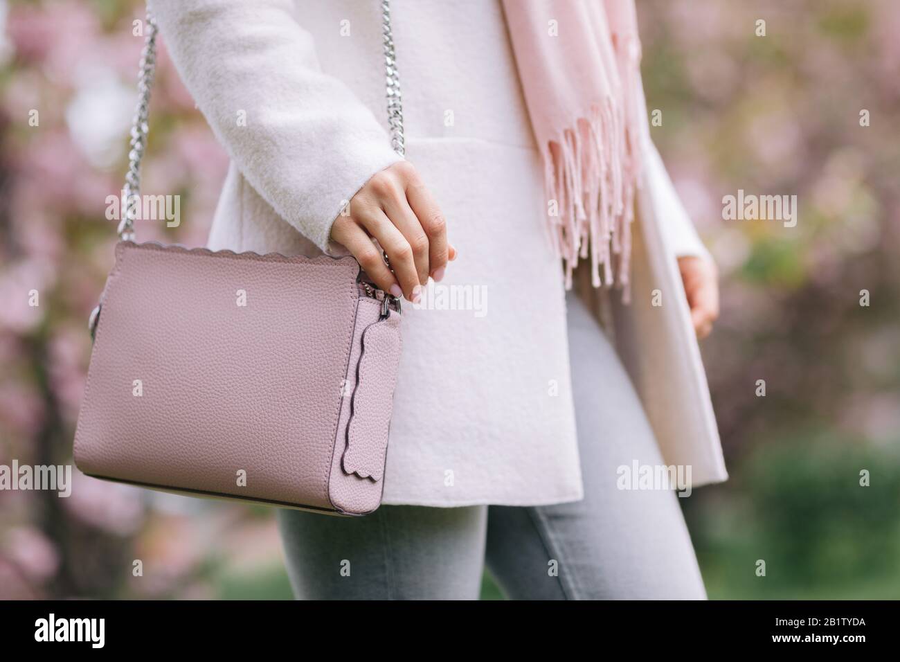 femme en manteau blanc, écharpe et sac à main rose se posant dans le parc  avec des arbres de printemps fleuris Photo Stock - Alamy