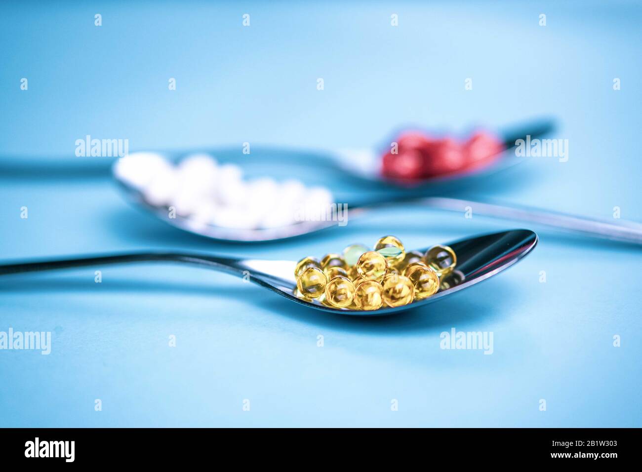 Cuillères avec pilules sur fond bleu clair. Concept de suppléments alimentaires sains. Banque D'Images