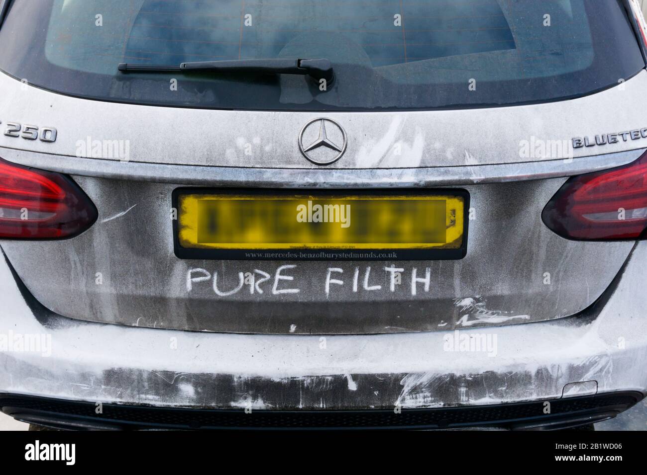 Les mots Pure Filth écrits dans la saleté à l'arrière d'une voiture Mercedes Bluetec blanche. Banque D'Images