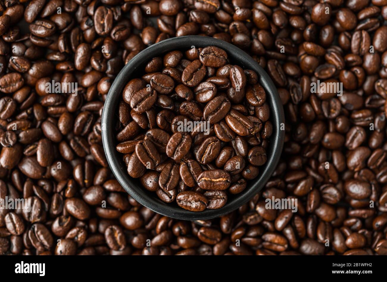 Grains de café rôtis dans un bol noir. Banque D'Images
