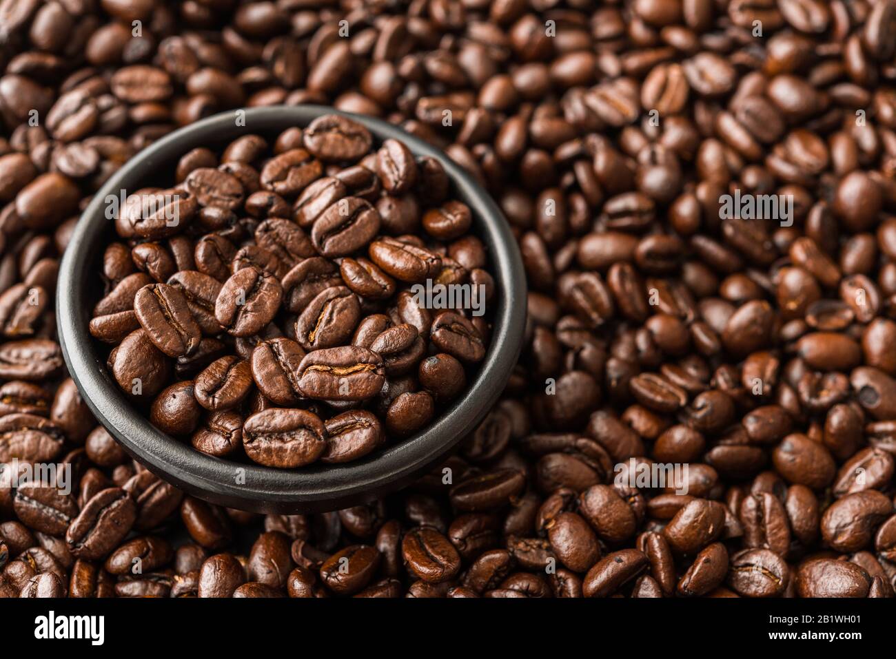 Grains de café rôtis dans un bol noir. Banque D'Images