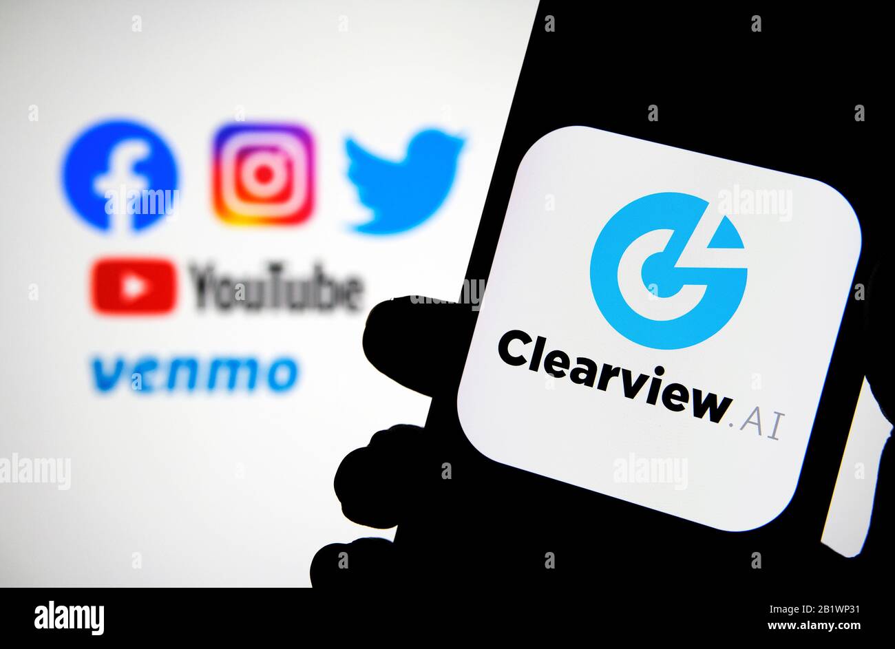 Le logo Clearview ai de la société sur le smartphone se tient entre les mains avec des réseaux sociaux flous où les données ont été recueillies. Concept de logiciel de reconnaissance faciale. Banque D'Images