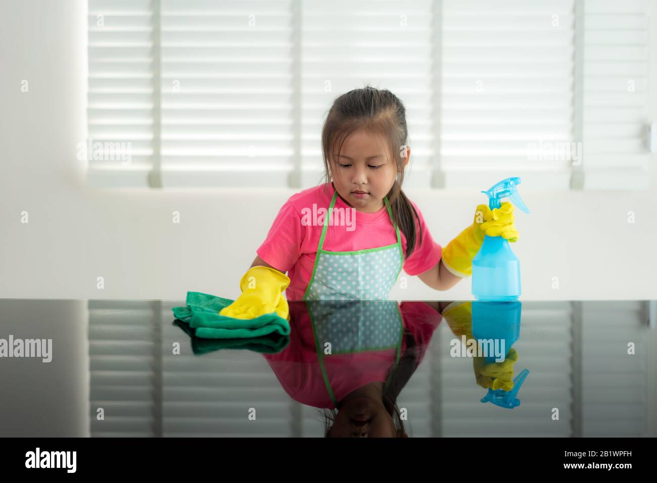 Cute asiatique fille étudiant préscolaire lave-table en verre avec une serviette verte dans la salle de séjour à la maison, avec de l'eau et d'une solution détergente pulvérisée. Banque D'Images