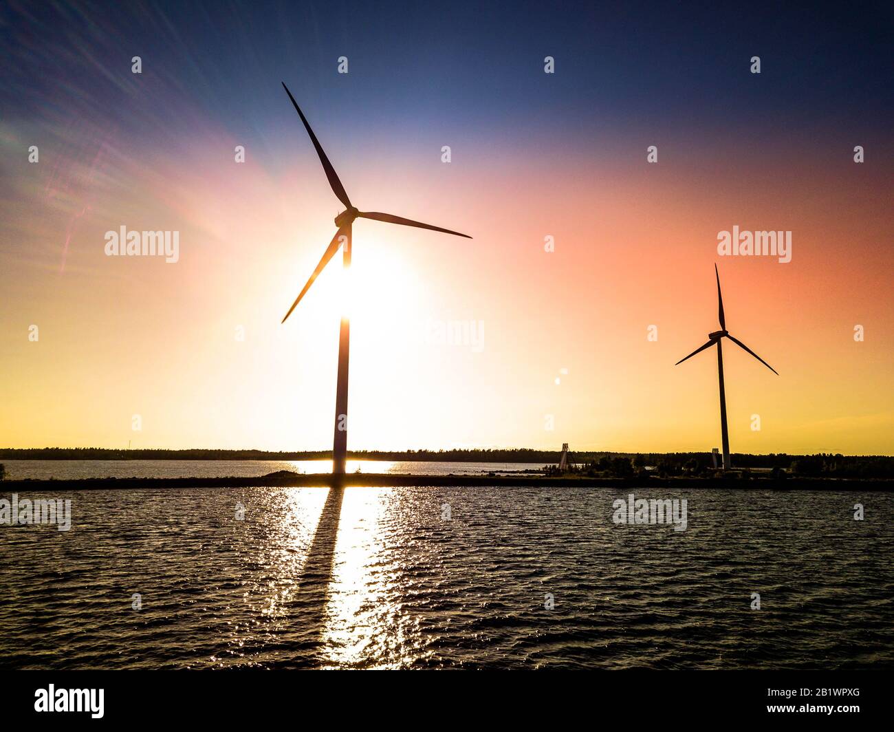 Photo aérienne de drone de deux moulins à vent debout sur la jetée de mer avec un coucher de soleil coloré derrière eux, des ombres sont vues sur la surface de mer ondulée. Suède Banque D'Images