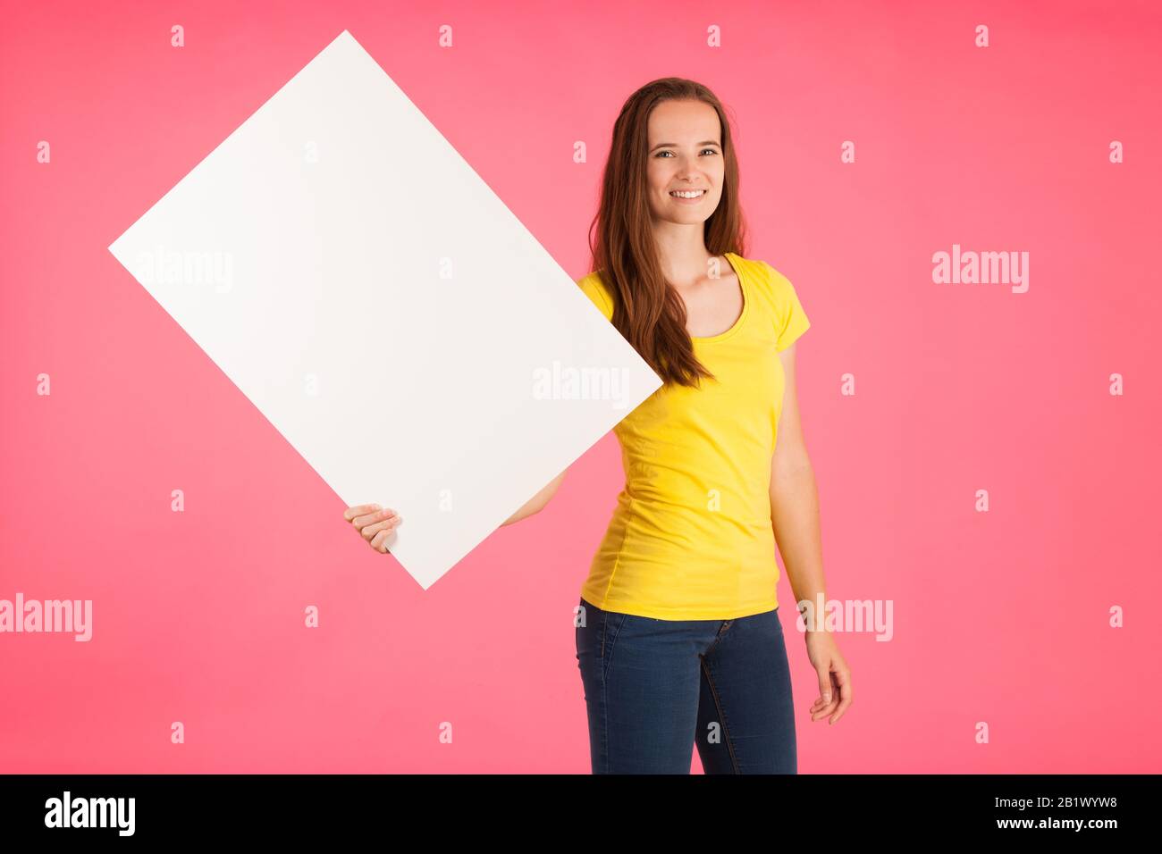 Jeune femme en t-shirt jaune tient une bannière vierge pour l'annonce sur fond rose vif Banque D'Images