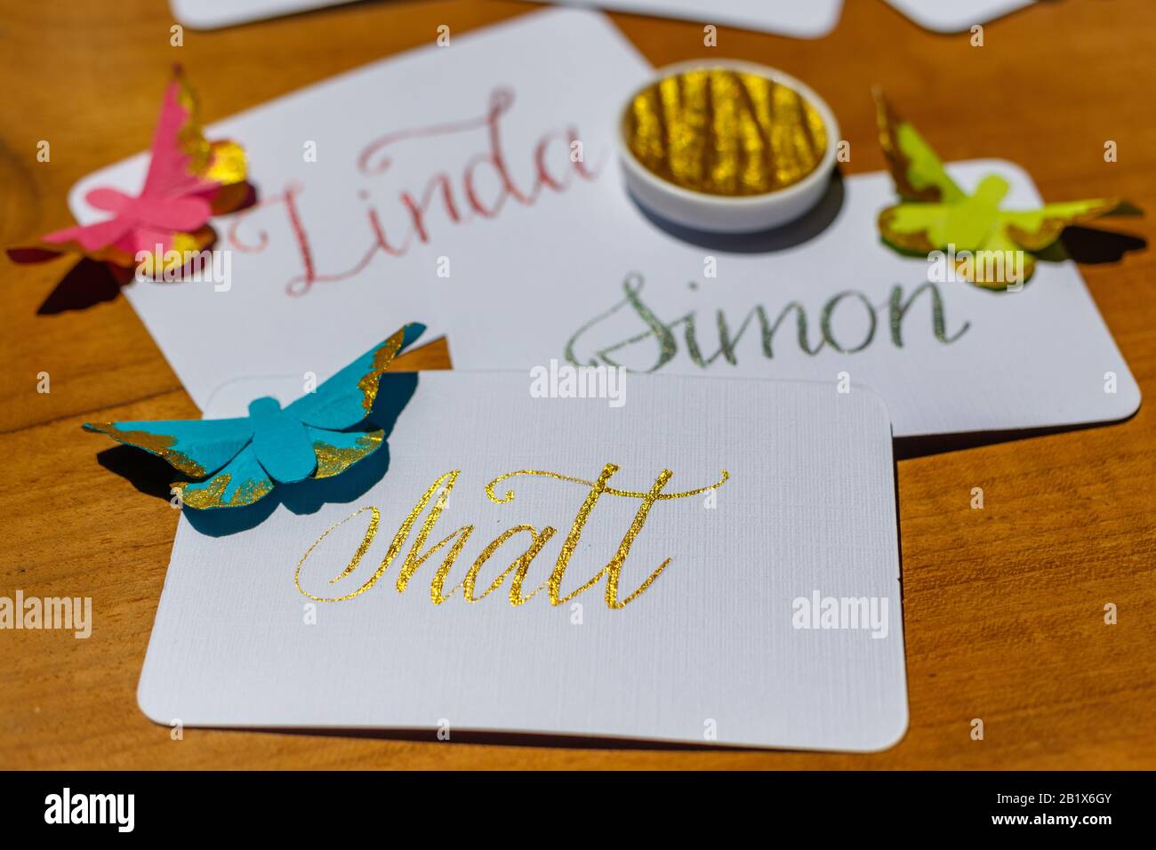 Calligraphie de mariage - cartes de lieu manuscrites avec des noms et des papillons en papier. Écriture dorée sur papier blanc. Banque D'Images