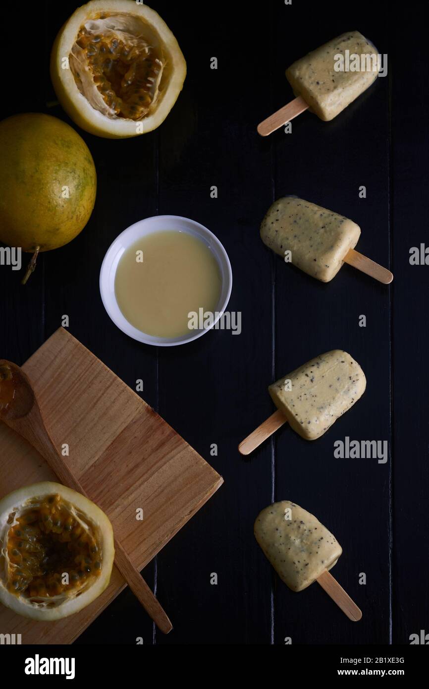 Glace aux fruits de la passion avec du lait condensé dans une tasse et des morceaux de fruits de la passion avec de la pâte et de la planche à découper sur carton noir en bois Banque D'Images