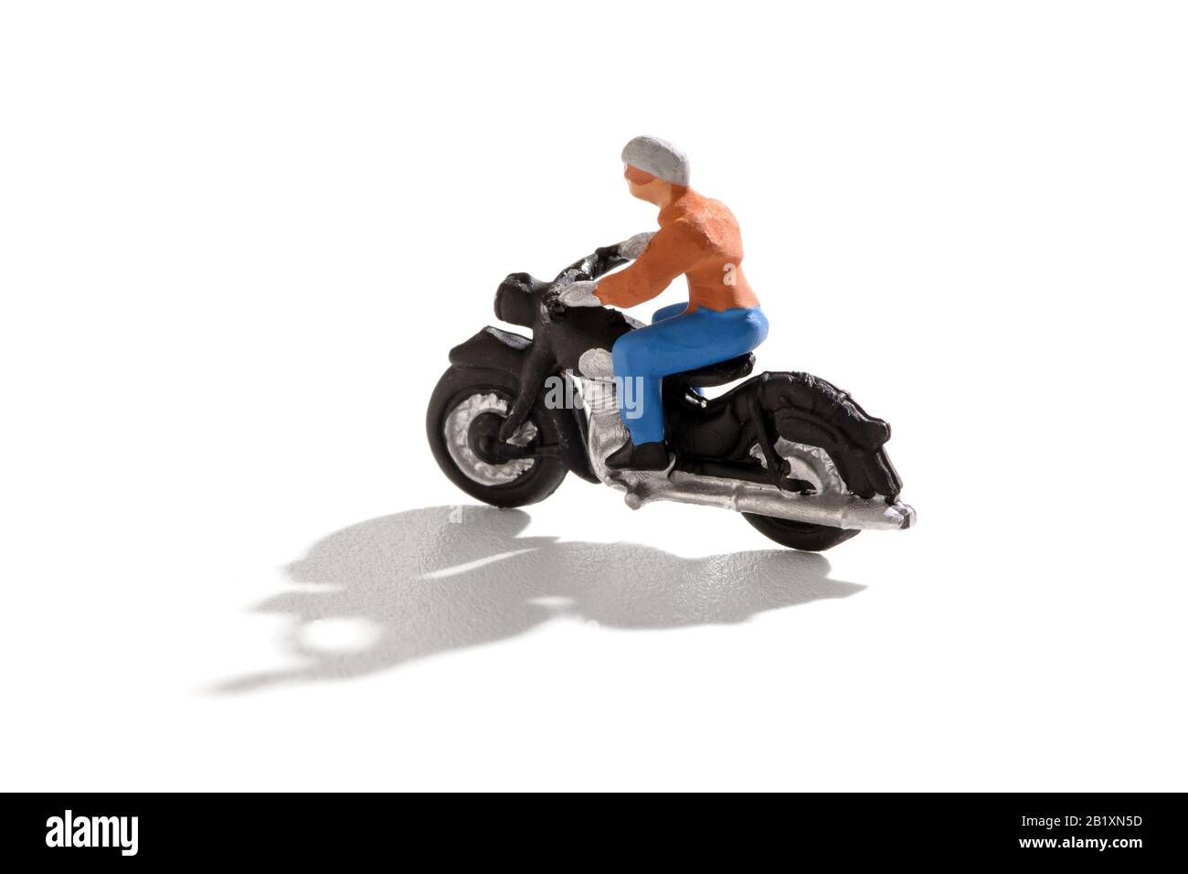 Personne miniature qui monte une moto avec ombre sur un fond blanc en vue latérale et espace de copie Banque D'Images
