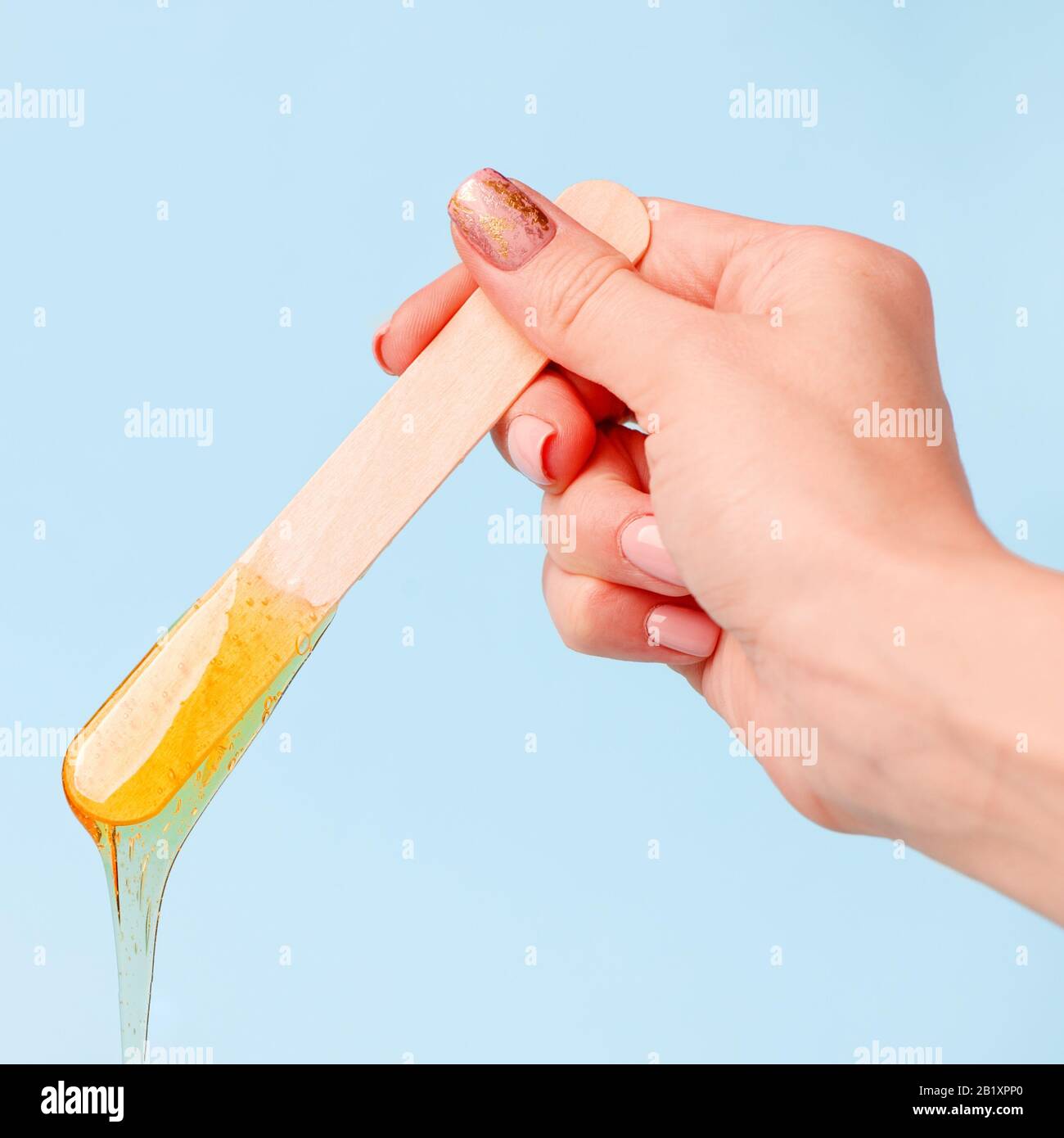 Main tenant cire de beauté ou pâte sugark sur la spatule en bois qui coule dans le récipient sur fond bleu. Publicité de la beauté concept de l'industrie, le luxe Banque D'Images
