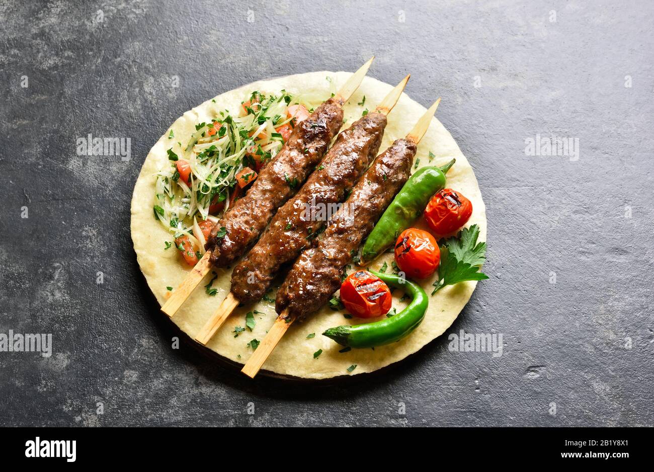 Adana Kebab turque avec des légumes frais sur du pain plat sur fond de pierre noire. Vue rapprochée Banque D'Images