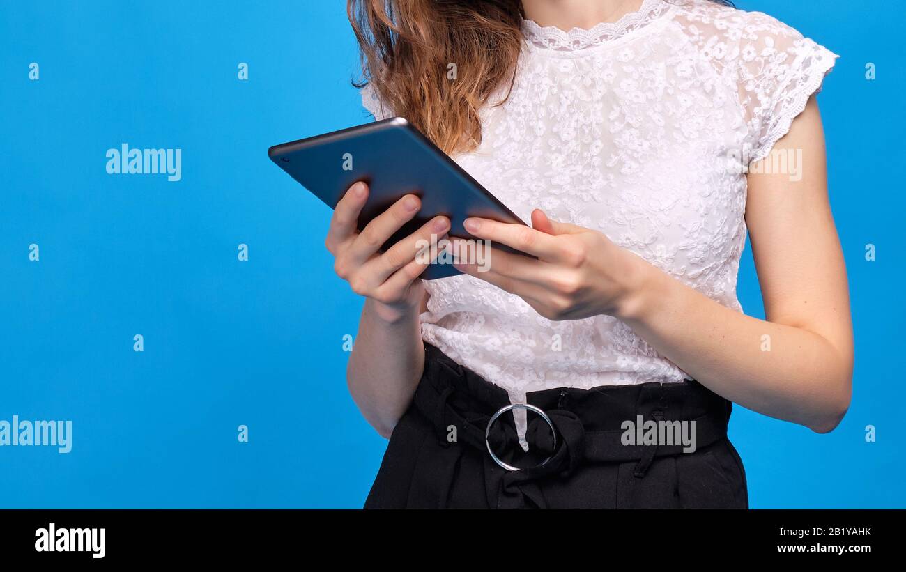 Une fille sans visage dans un cadre dans des vêtements décontractés sur un fond bleu tient une tablette. Gros plan. Banque D'Images