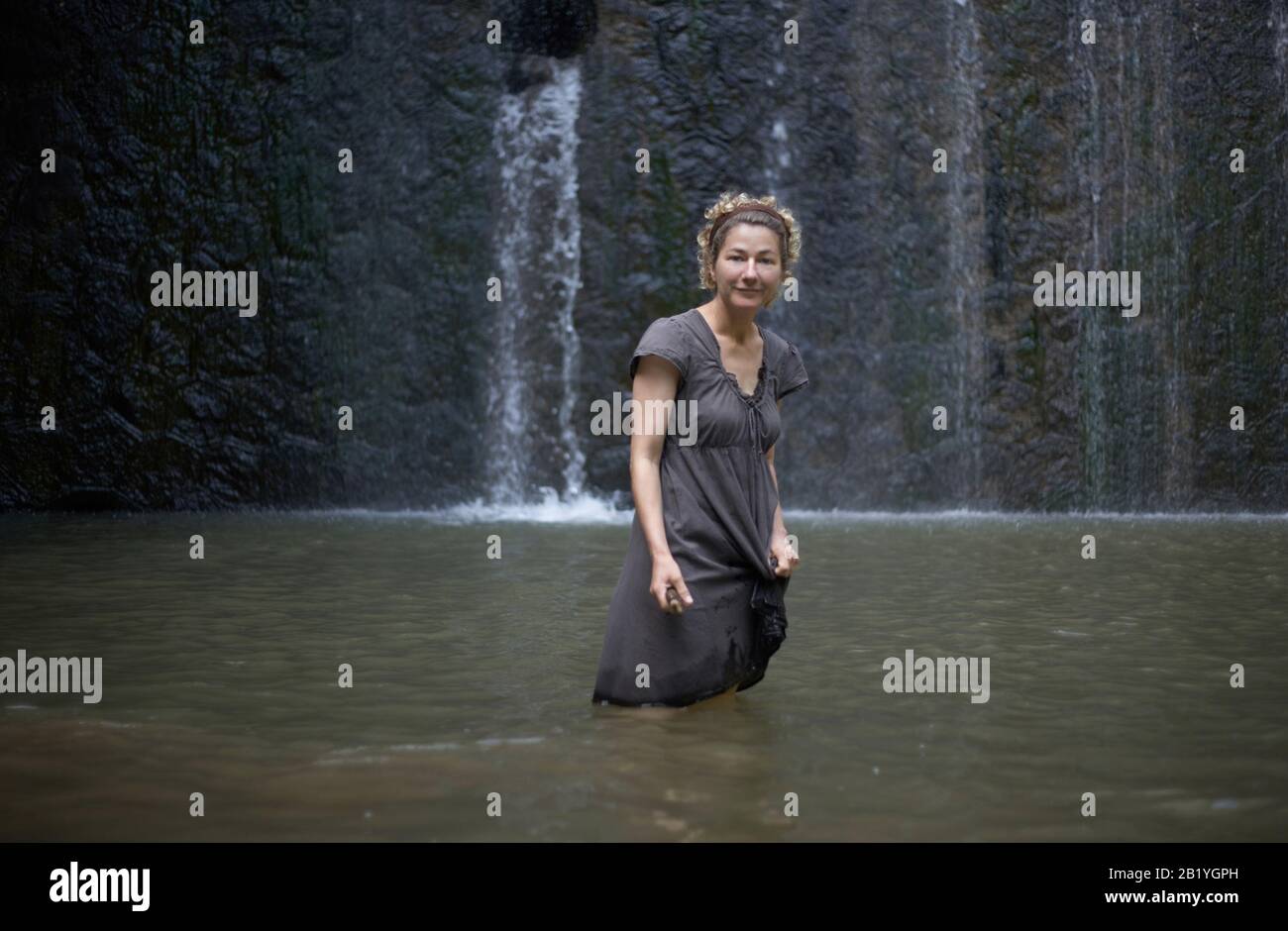 Femme souriante et détendue, en plein été, se tenant dans l'eau d'une cascade rocheuse Banque D'Images