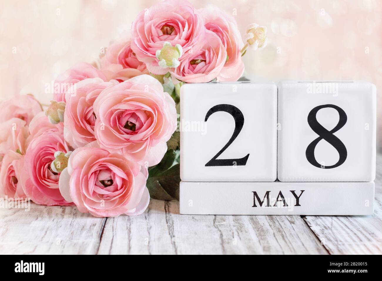 Blocs calendrier en bois blanc avec la date 28 mai et fleurs roses de ranunculus sur une table en bois pour le jour commémoratif national. Mise au point sélective avec flou Banque D'Images