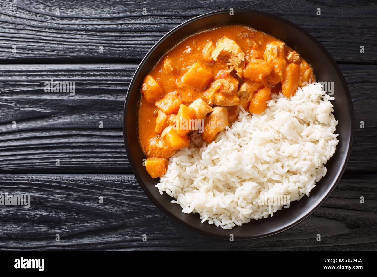 Domoda de ragoût africain avec des arachides cuites avec de la citrouille de poulet et servies avec un gros plan de riz dans une assiette sur la table. Vue de dessus horizontale Banque D'Images