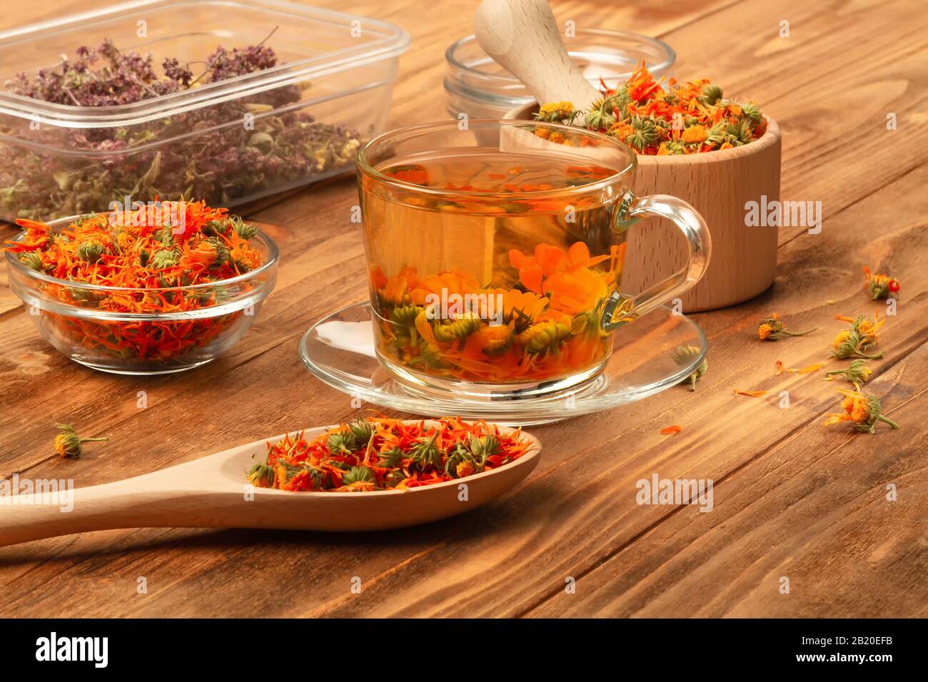 Mortier en bois avec fleurs thérapeutiques de calendula sèche, rosette avec calendula, tasse de thé avec fleurs de calendula sur une table en bois. Banque D'Images