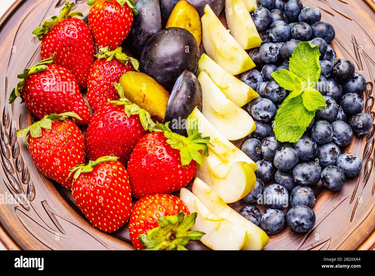 Fruits crus baies assiette, pomme, fraise, bleuet, prune, menthe. Sur la plaque de céramique ethnique, concept sain de nourriture végétarienne (végétalienne). Béton de pierre Banque D'Images