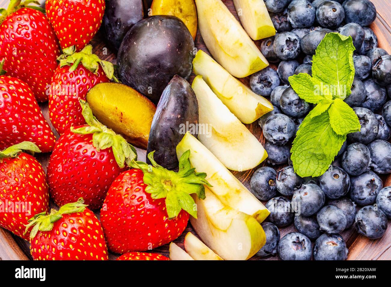 Fruits crus baies assiette, pomme, fraise, bleuet, prune, menthe. Sur la plaque de céramique ethnique, concept sain de nourriture végétarienne (végétalienne). Béton de pierre Banque D'Images