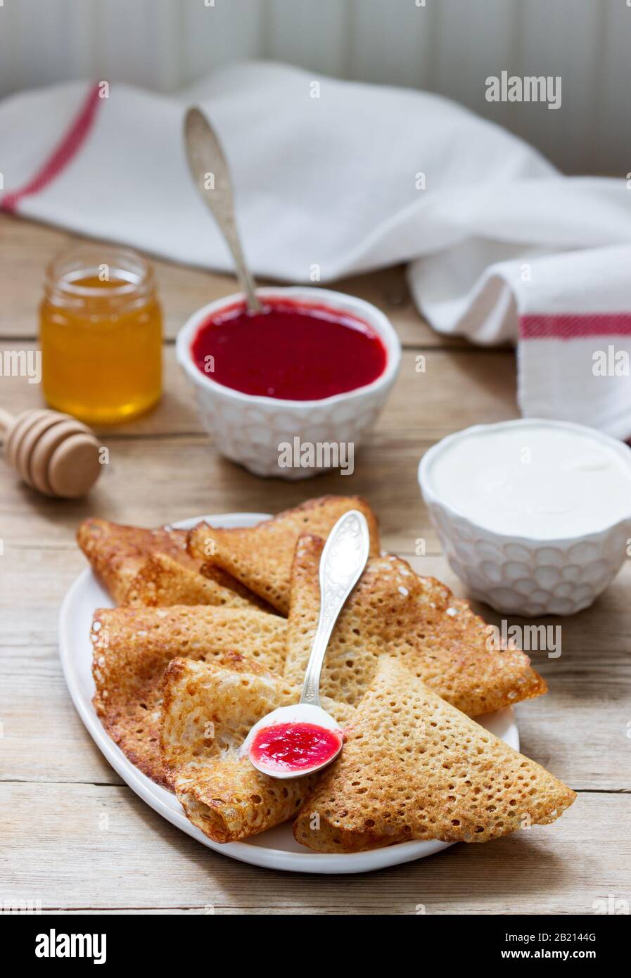 Crêpes au seigle et au grain entier servies avec de la crème aigre, du miel et de la sauce aux fraises. Style rustique. Banque D'Images
