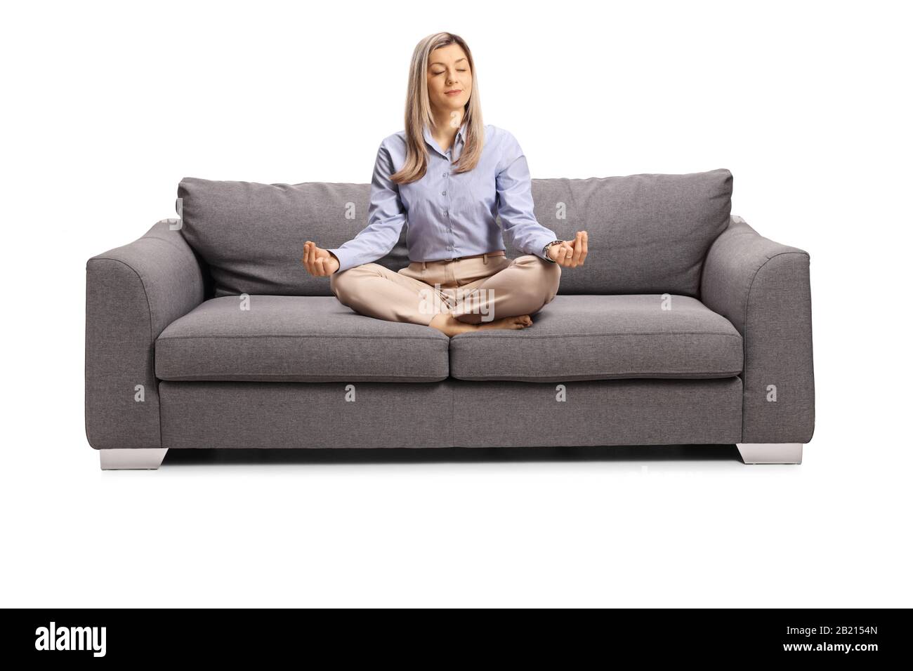 Jeune femme en vêtements formels assis sur un canapé avec des jambes croisées dans une méditation pose isolée sur fond blanc Banque D'Images