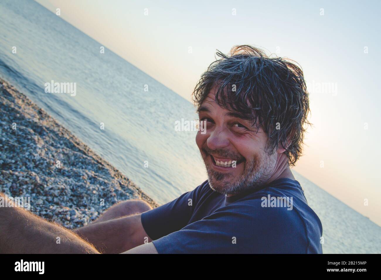 Bel homme se reposant sur la plage en Grèce alors que couchers de soleil / Portrait de beau homme d'âge moyen Banque D'Images