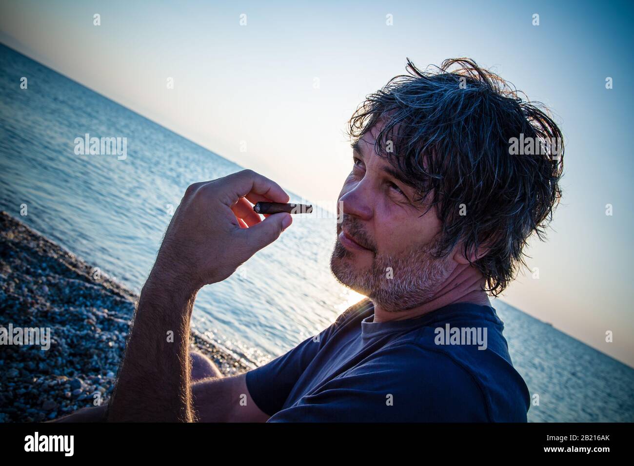 Charmant homme d'âge moyen avec un siège de cigare sur la plage tandis que couchers de soleil / gros portrait Banque D'Images