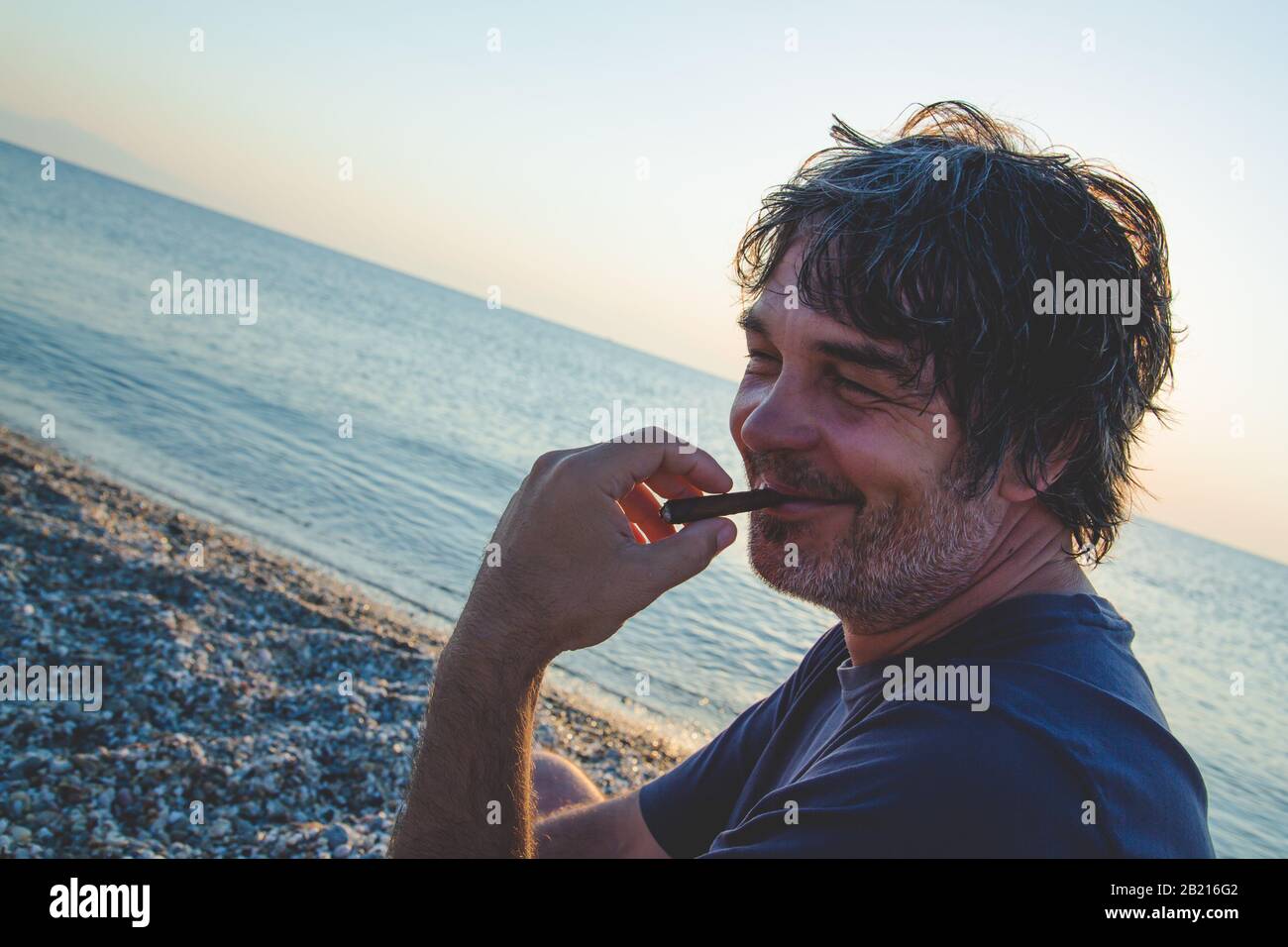 Charmant homme d'âge moyen avec un siège de cigare sur la plage tandis que couchers de soleil / gros-up portraitsouriant Banque D'Images